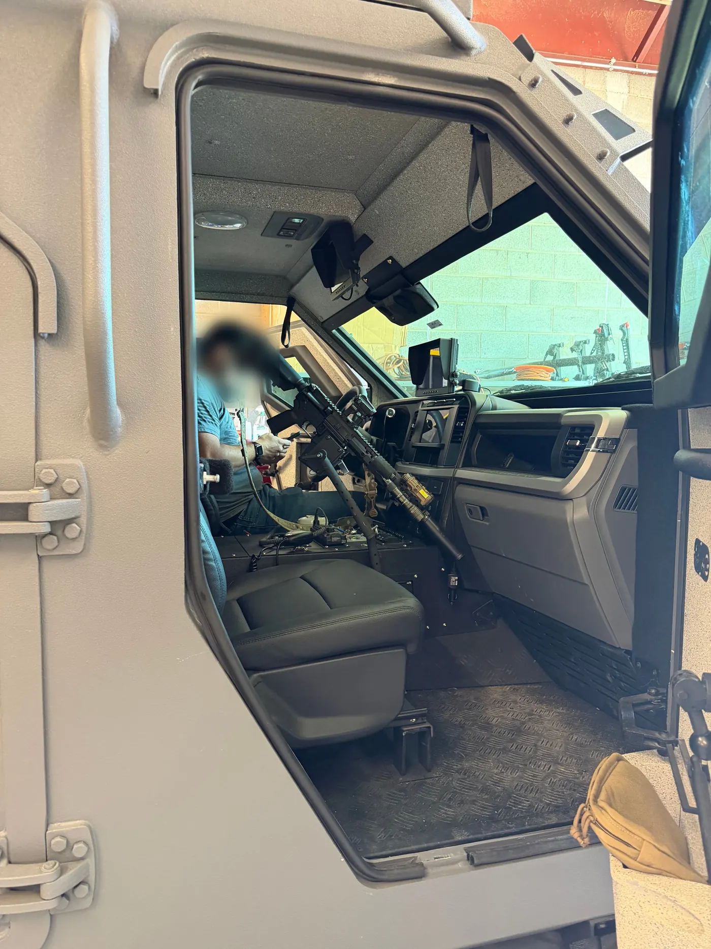 View through the open armored door of an IAG Sentinel: StandA.R.D. mounted with the rifle staged within reach of the driver's seat
