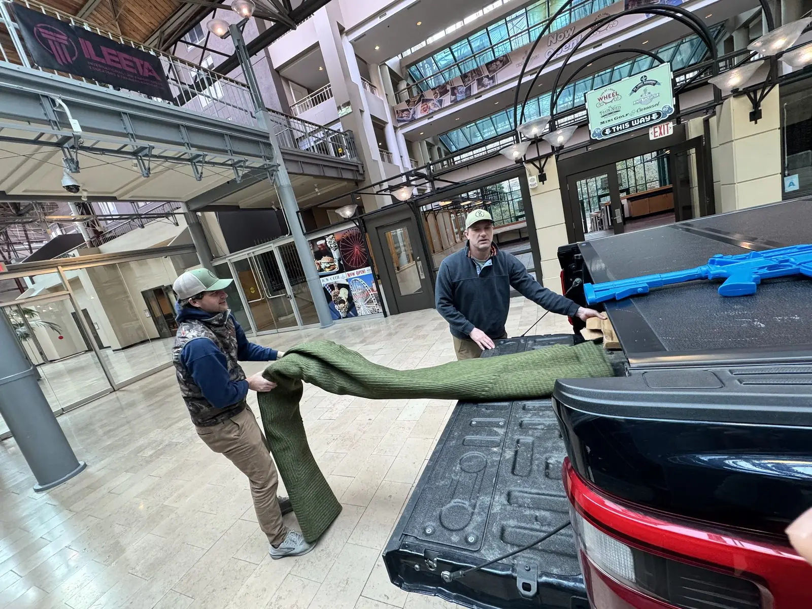 Two Pl8tek staff unrolling display turf from a truck bed under the ILEETA sign.
