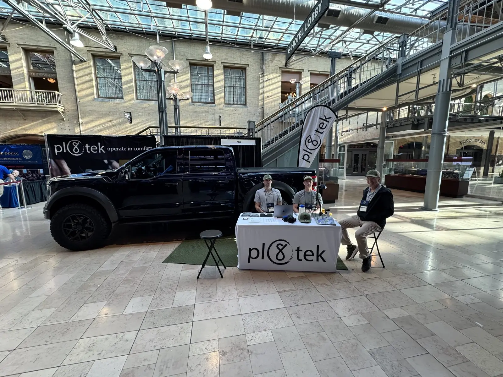 Pl8tek staff seated at the booth table talking with attendees.
